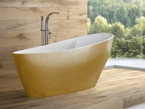 Złota wanna wolnostojąca Besco Keya Glam 165x70 w łazience z drewnianym wykończeniem i widokiem przez okno na las.