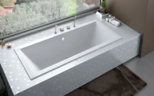 Nowoczesna wanna prostokątna Besco Quadro Slim w białej zabudowie z mozaiki w luksusowej aranżacji łazienki.