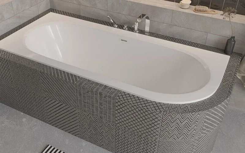 Besco Avita Slim Plus Wanna asymetryczna Besco Avita Slim Plus lewa z przelewem szczelinowym w obudowie z mozaiki i łazience z drewnianą podłogą.