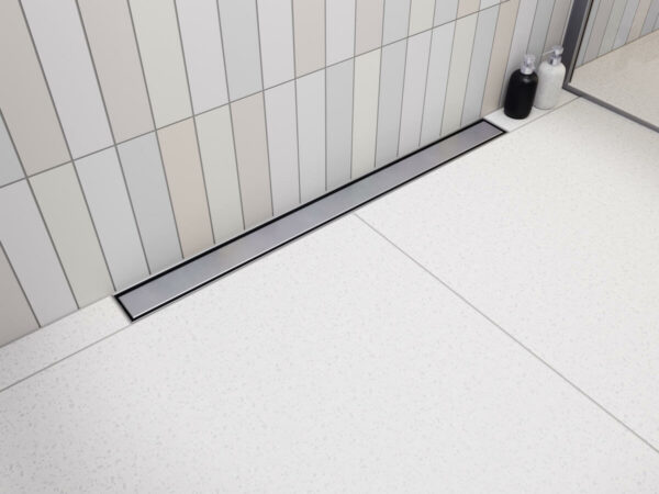 Elegancki odpływ przyścienny Vogi Premium SLX z gładkim rusztem ze szczotkowanej stali inox w jasnej aranżacji łazienki.