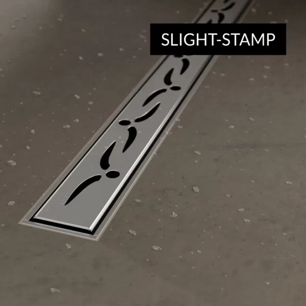Zbliżenie na ozdobną maskownicę Stamp wąskiego odpływu liniowego Schedline Slim wklejonego w płytki