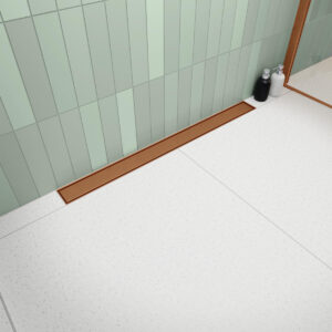 Nowoczesna kabina prysznicowa z zamontowanym miedzianym odpływem przyściennym Vogi o gładkim, szczotkowanym ruszcie na tle zielonych kafelków.